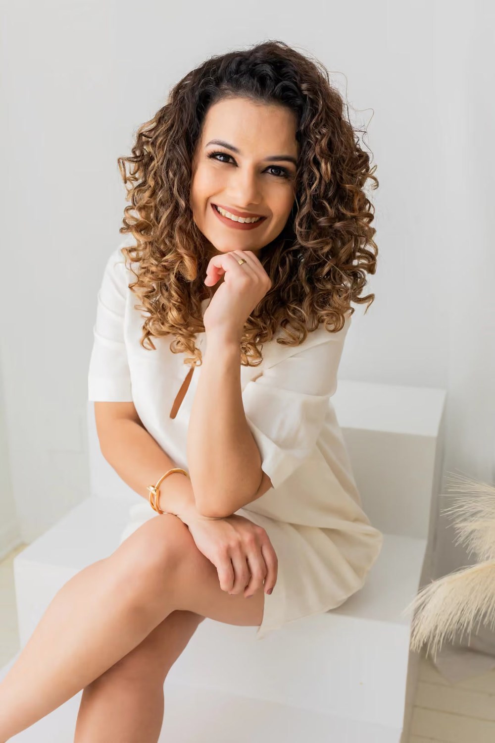 Monik Santana sorrindo, sentada, em estúdio de fundo claro